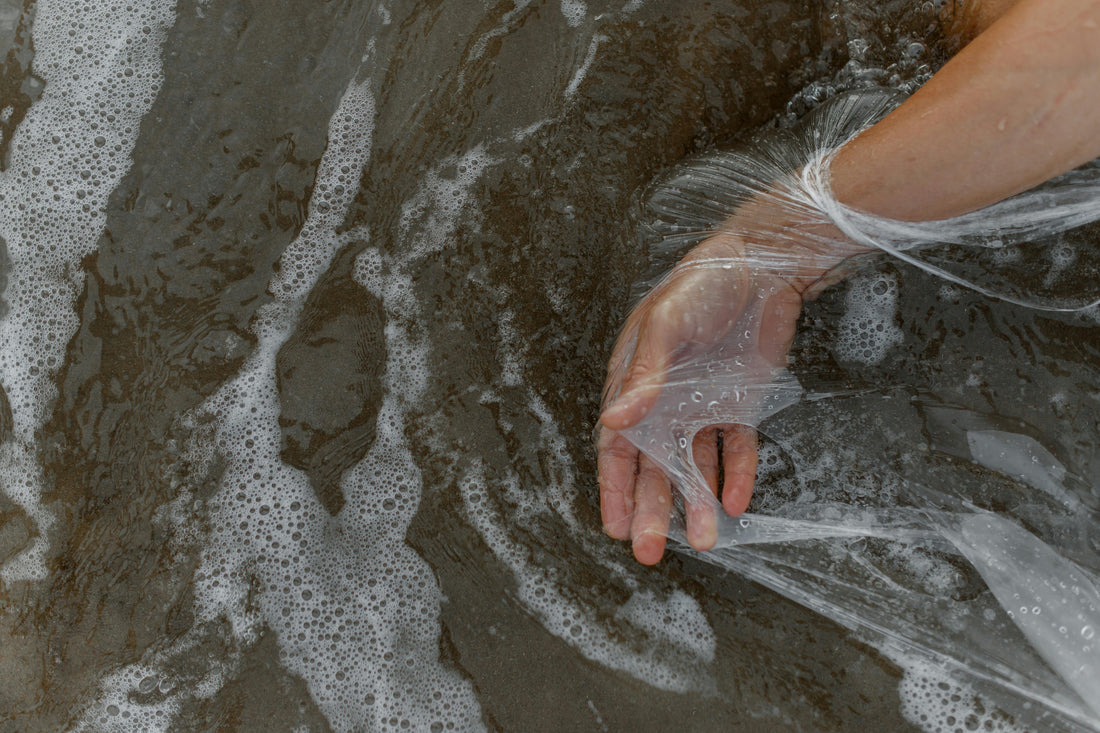 Hand pushing through plastic into the sea