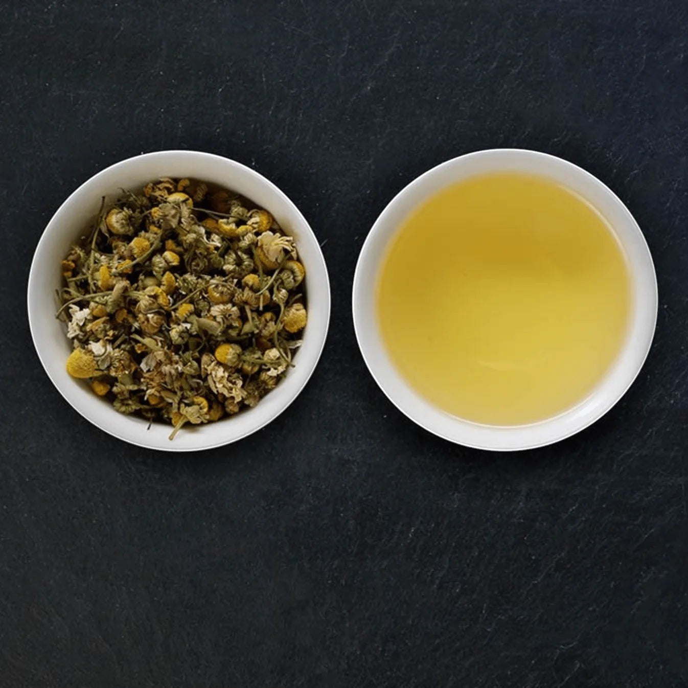 Good and Proper Tea chamomile tea featuring dried flowers in a bowl next to a cup of golden herbal tea on a dark slate background