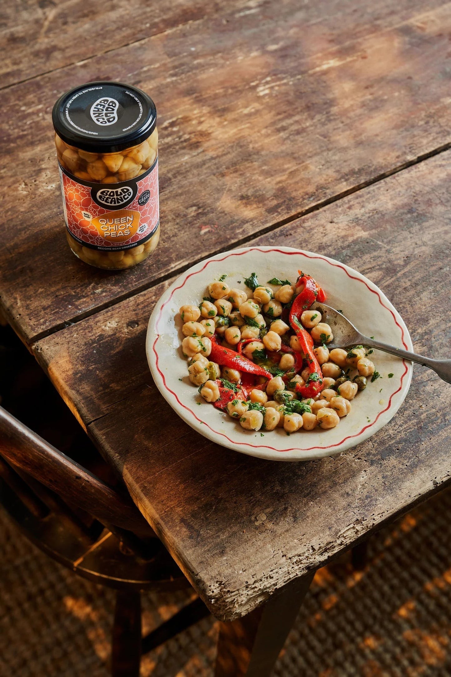 Bold Bean Co Queen Chickpeas jar next to a rustic bowl of prepared heirloom chickpeas with roasted red peppers and herbs.