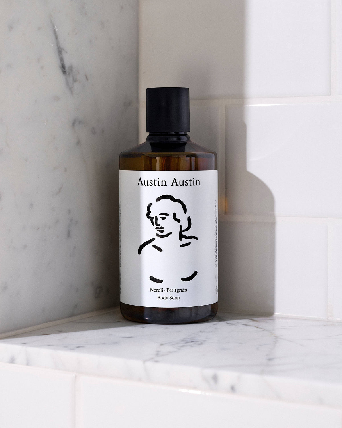 Austin Austin Neroli & Petitgrain body soap in an amber glass bottle with artistic ink illustration on a marble surface.