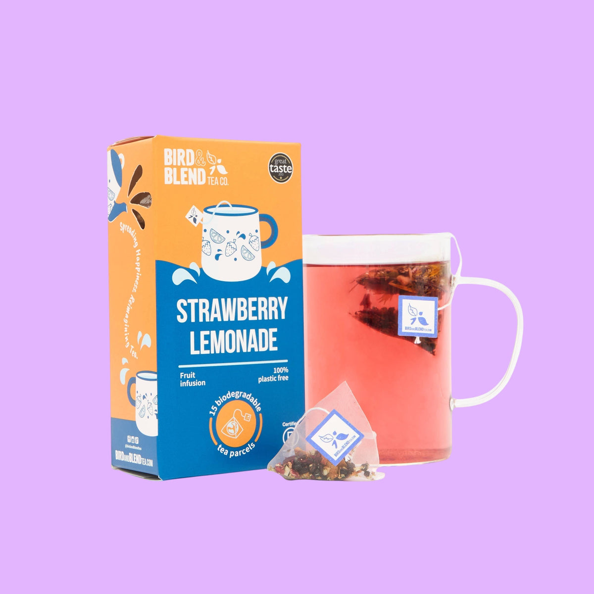 Bird and blend Strawberry Lemonade fruit tea box with a glass mug of pink tea and a biodegradable pyramid tea bag, shown from a different angle.