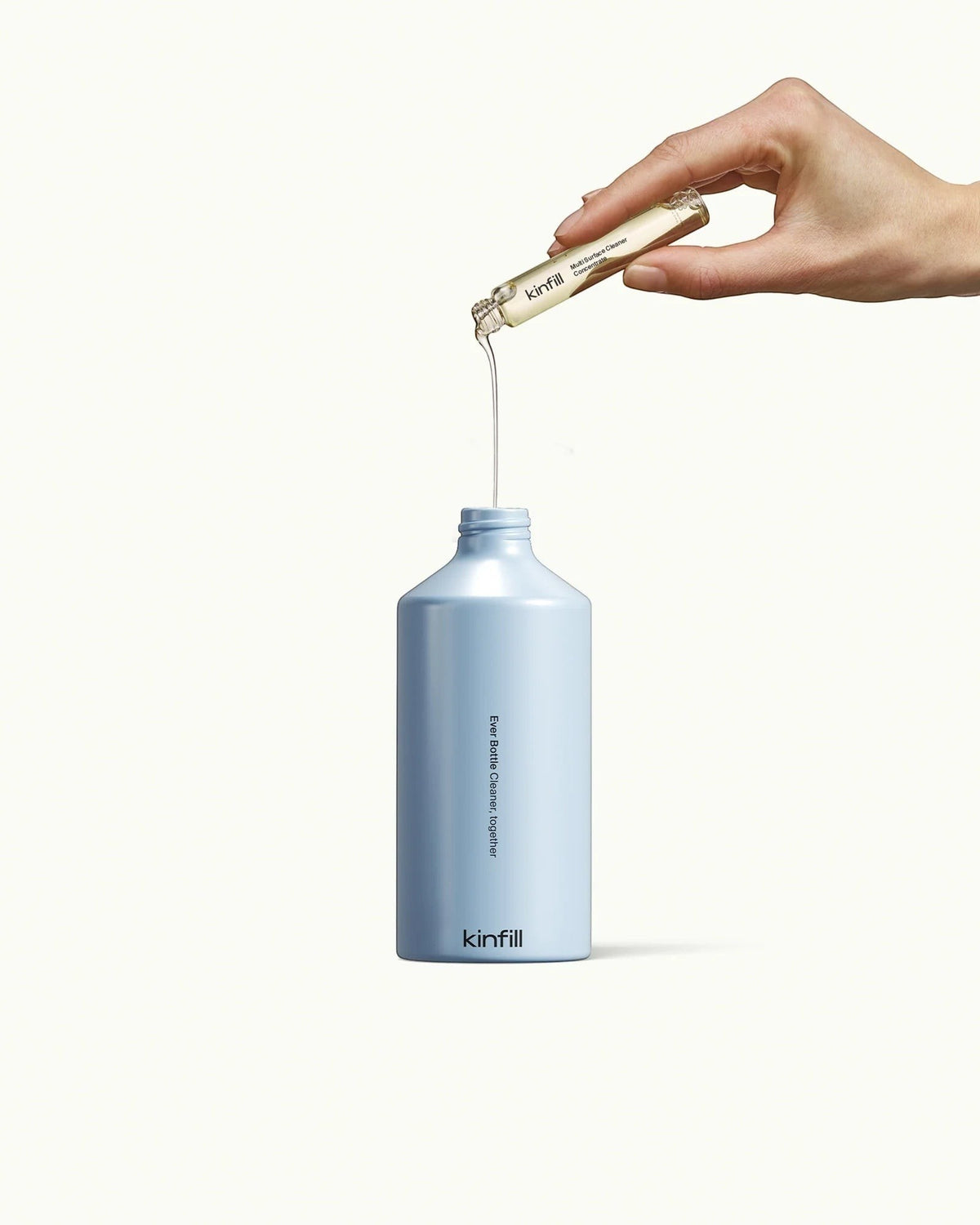 Kinfill multi surface cleaner refill vial being poured into a light blue reusable spray bottle