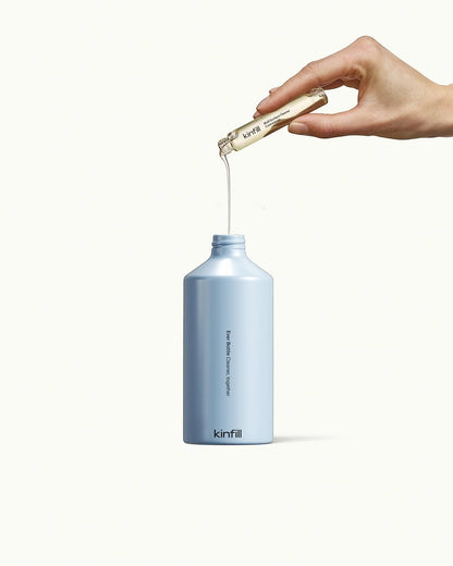 Kinfill multi surface cleaner refill vial being poured into a light blue reusable spray bottle