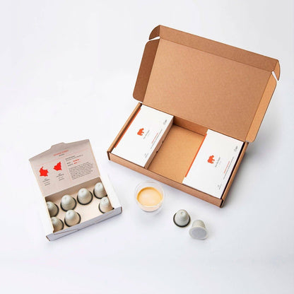 Kiss the Hippo organic coffee pods in compostable packaging with a small glass of espresso on a white background