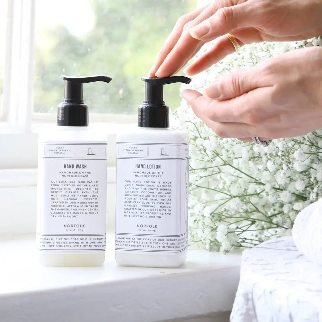 Norfolk Natural Living Coastal Walks hand wash and lotion set in white bottles with pump dispensers on a windowsill with flowers