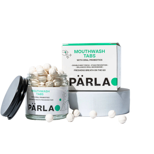 Pärla Mouthwash Tabs with oral probiotics shown with an open jar of white tablets, a black lid, the product box, and a few loose tablets on a clean white studio background.