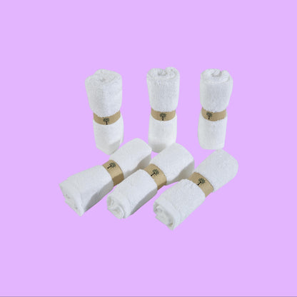 Re:gn set of six white organic bamboo face cloths rolled and secured with eco-friendly paper bands, shown from a different angle.