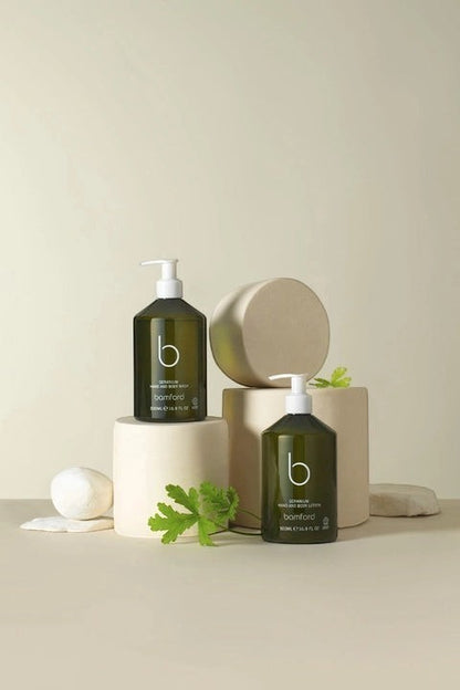 Bamford Geranium hand and body lotion in a dark green pump bottle displayed on minimalist beige pedestals.