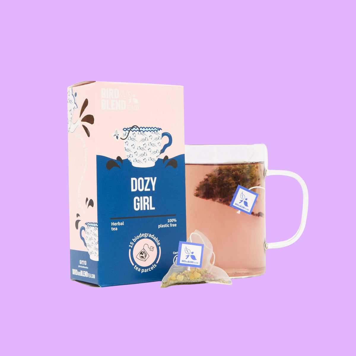 Bird and Blend Dozy Girl chamomile herbal tea box with a glass mug of tea and a biodegradable tea bag on a purple background