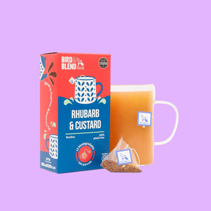 Bird and Blend Rhubarb & Custard tea box with a biodegradable tea bag and a glass mug of brewed rooibos tea.
