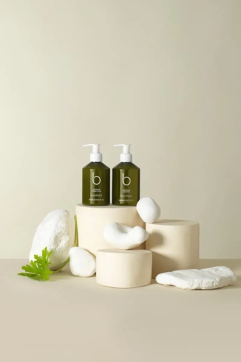 Bamford organic shampoo and conditioner duo in green bottles with pump dispensers on decorative stone pedestals.
