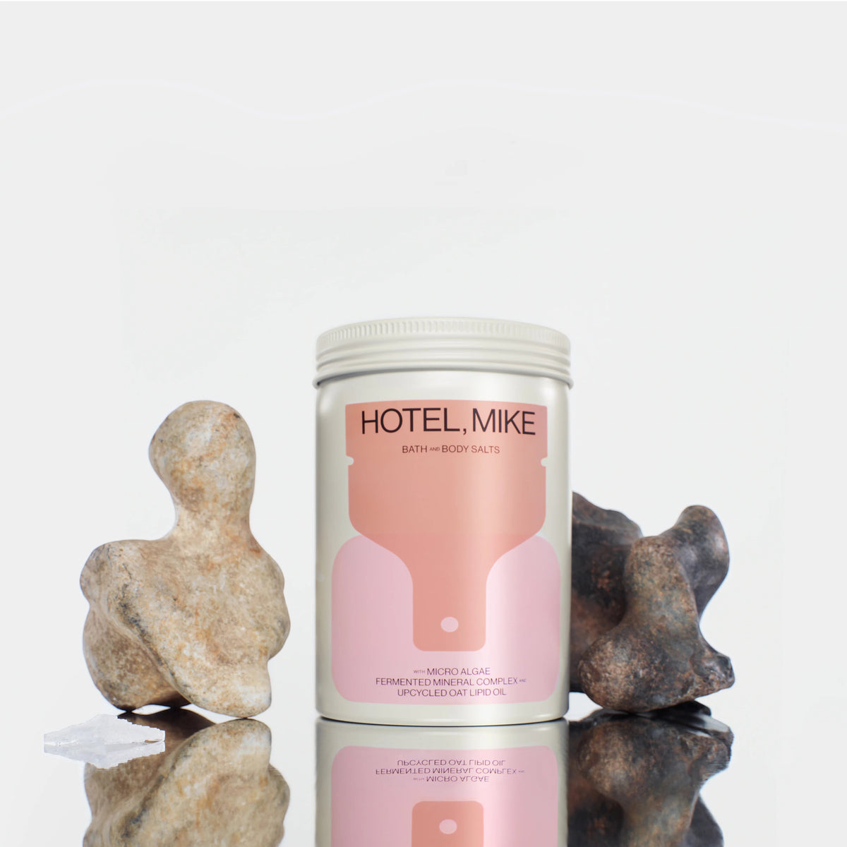 Hotel Mike Bath and Body Salts in a sustainable jar with pink label, displayed with decorative stones on a reflective base.