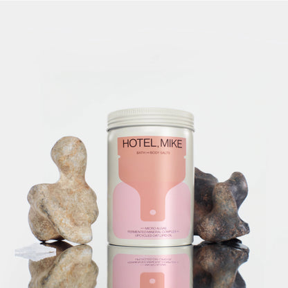 Hotel Mike Bath and Body Salts in a sustainable jar with pink label, displayed with decorative stones on a reflective base.
