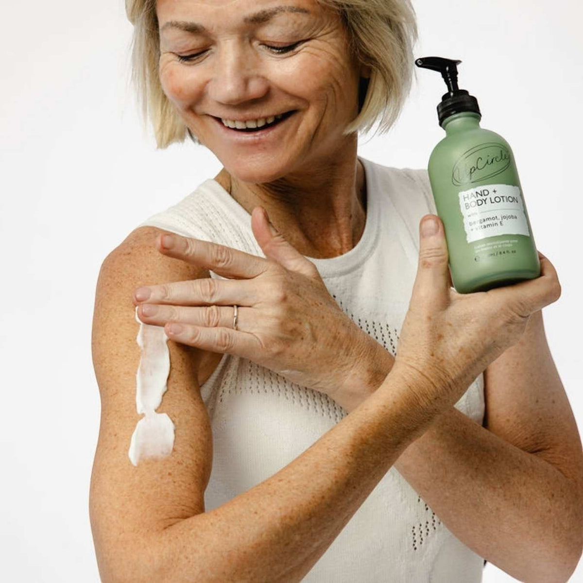 UpCircle hand and body lotion in a frosted green glass bottle being applied to a woman's arm