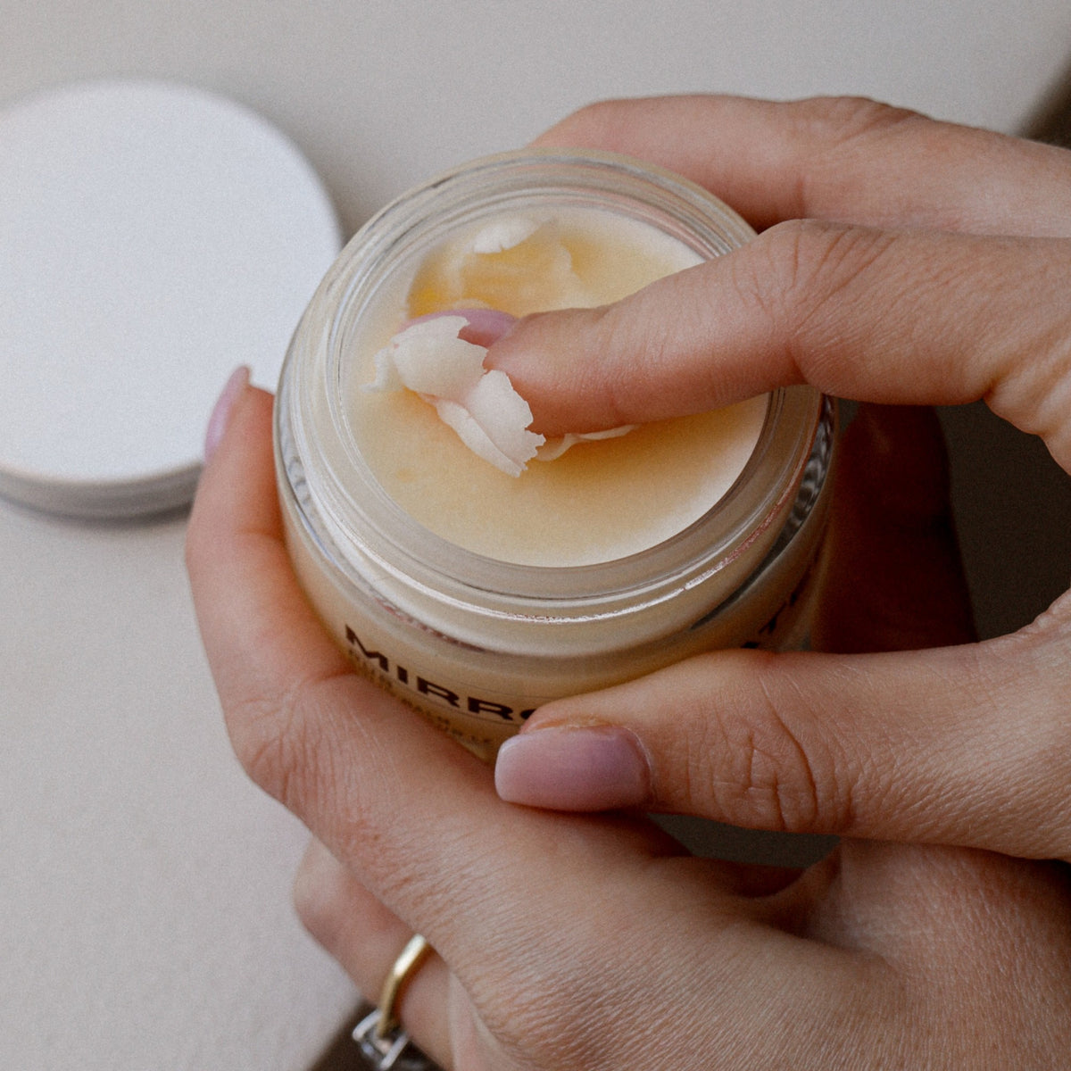 Mirror Water body balm in a glass jar being scooped with a finger, showing the dense shea butter texture.