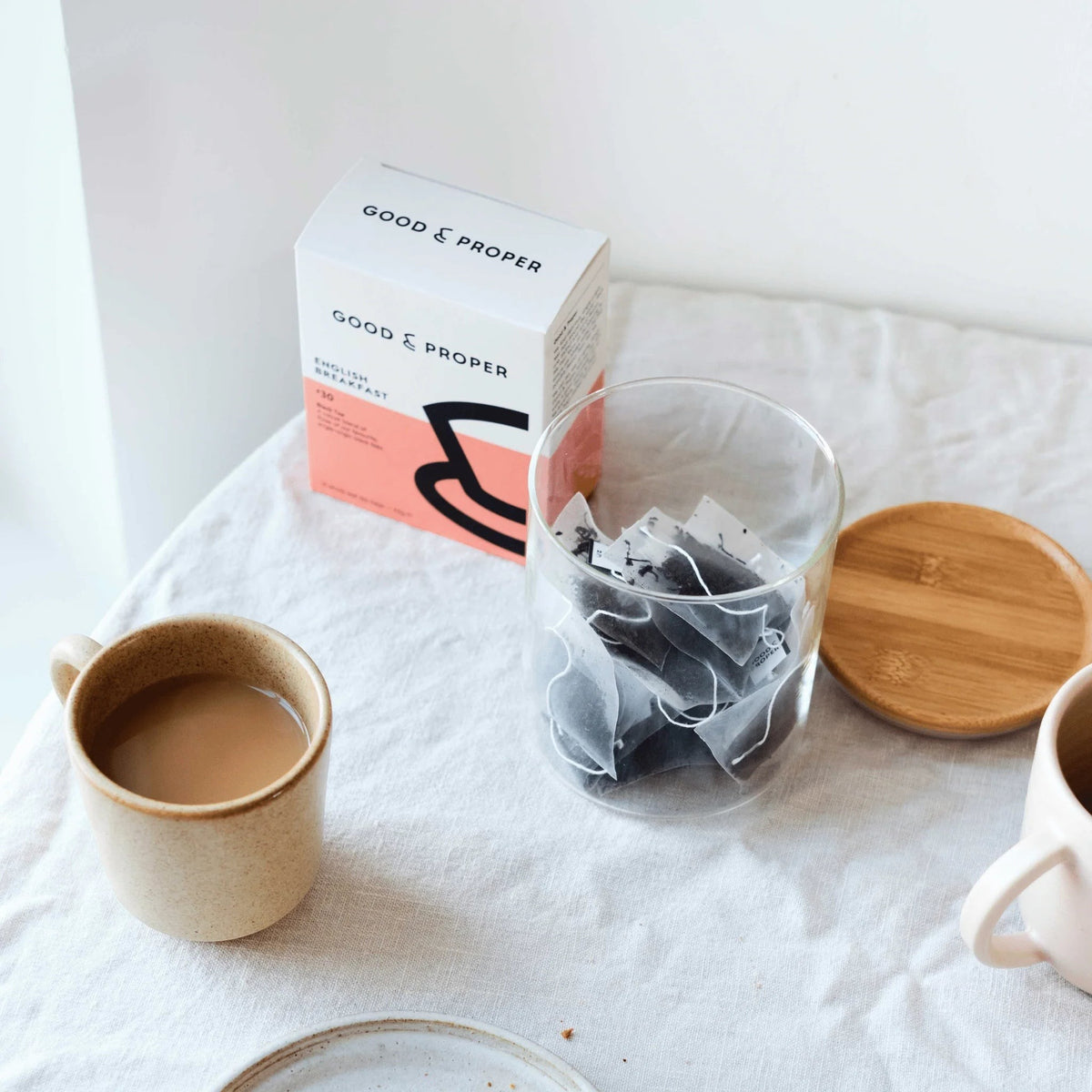 Good & Proper Tea Brockley Breakfast black tea bags in a glass jar next to a ceramic mug on a linen tablecloth