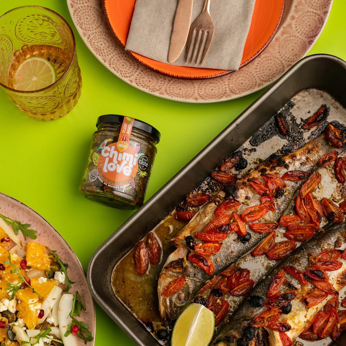 Chimi Love Chimichurri Medium Sauce jar next to a roasted fish dish with tomatoes and a fresh citrus salad