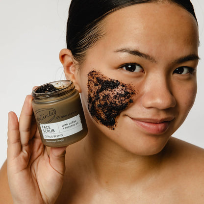 UpCircle face scrub with coffee and rosehip oil applied to a woman's cheek, held in a glass jar with an aluminium lid.