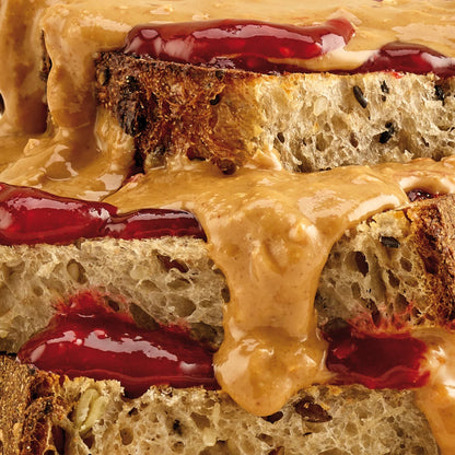 Pip & Nut Crunchy Peanut Butter spread over thick slices of seeded sourdough bread with red fruit jam