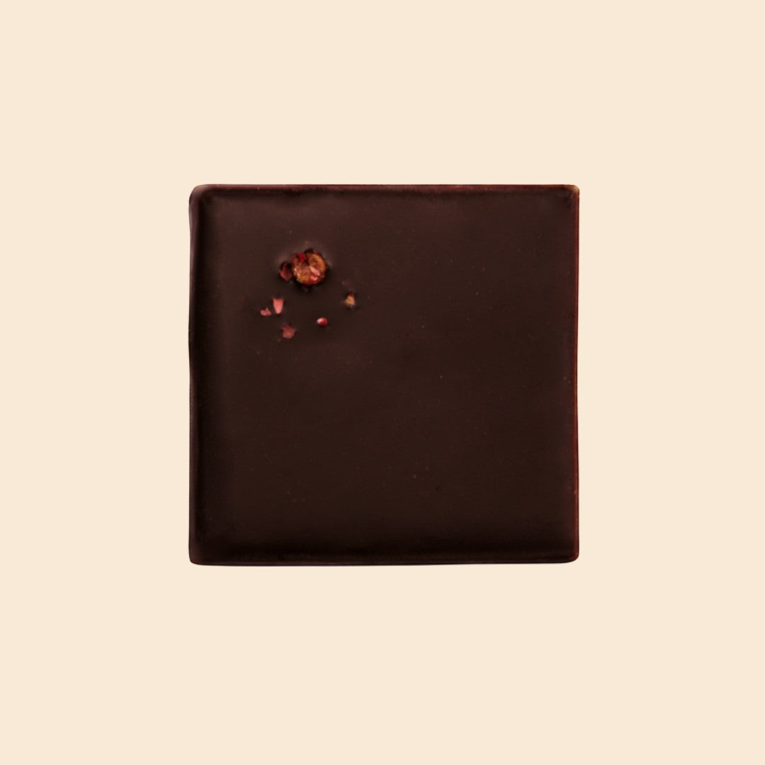 Cosmic Dealer dark chocolate square with macadamia nut butter and a garnish of dried raspberry pieces on a cream background.