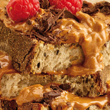 Pip & Nut dark roast crunchy peanut butter spread on sourdough toast topped with fresh raspberries and chocolate shavings