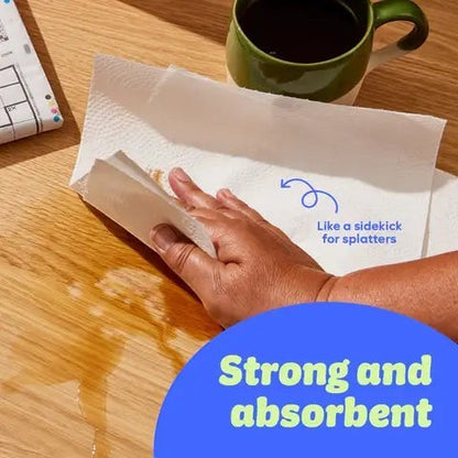 Who Gives A Crap double length kitchen roll being used to wipe up a spill on a wooden table next to a green mug