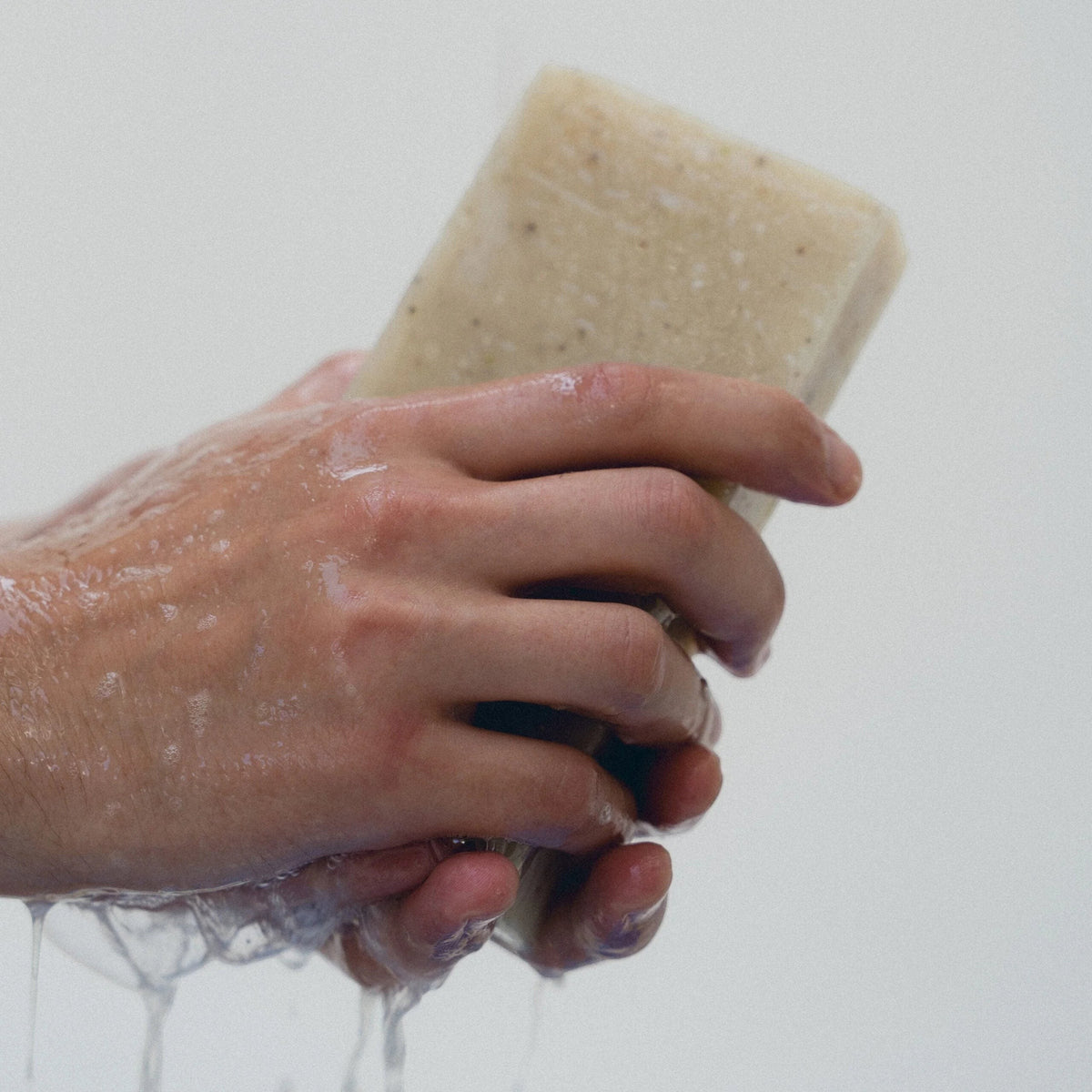 dulcie exfoliating seaweed block soap being held in wet hands, showing the textured surface and lather.