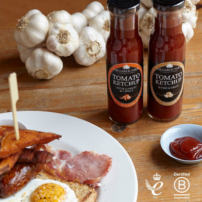 The Garlic Farm tomato ketchup with garlic bottles next to a breakfast plate with fresh garlic bulbs.