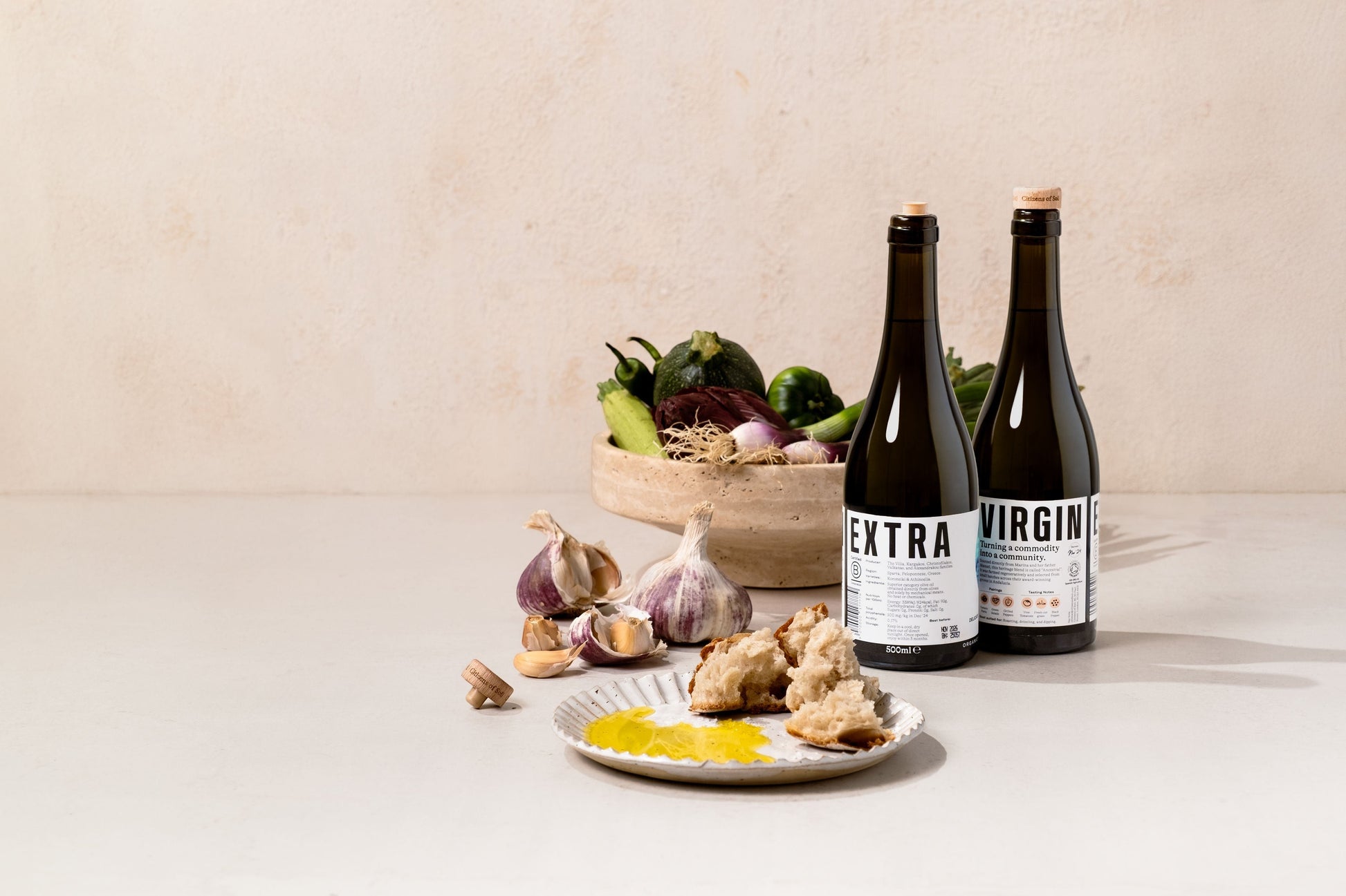 BRiMM Citizens of Soil Greek extra virgin olive oil bottles with fresh vegetables, garlic, and bread on a table