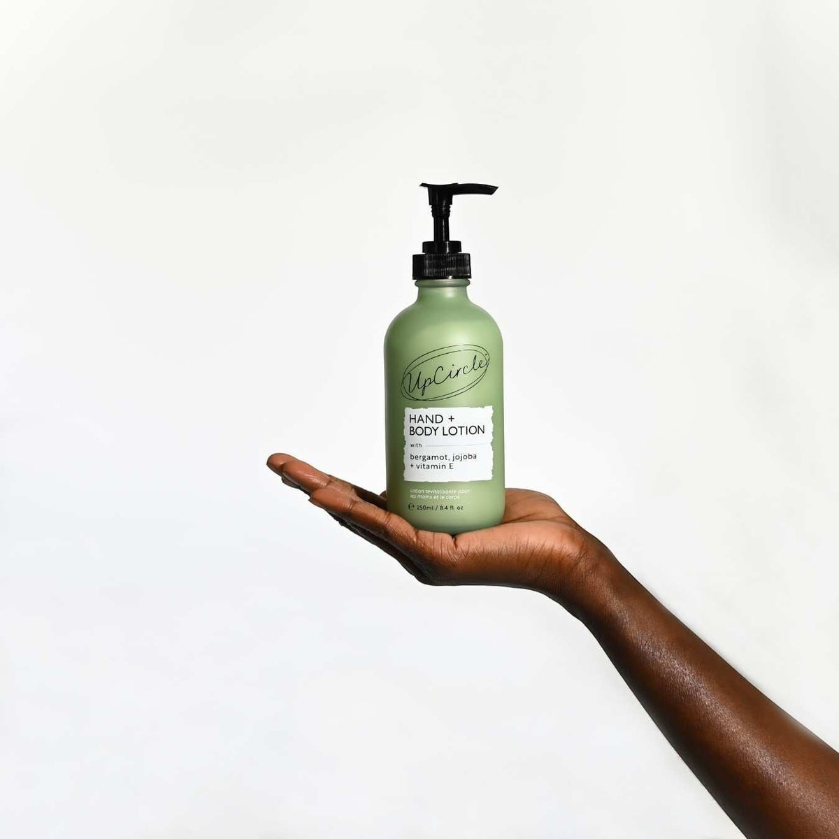 UpCircle hand and body lotion in a frosted green glass bottle with a pump dispenser held in a person's hand