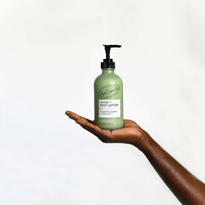 UpCircle hand and body lotion in a frosted green glass bottle with a pump dispenser held in a person's hand