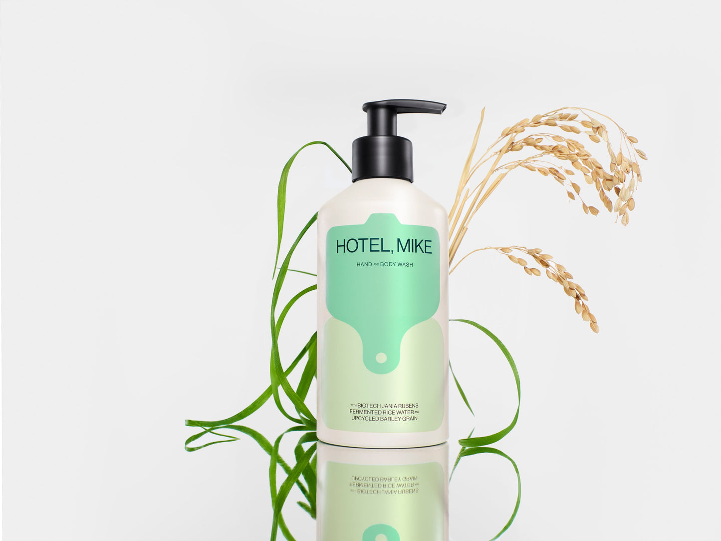 Hotel Mike Hand & Body Wash in a recyclable aluminium bottle with a pump dispenser, styled with rice stalks and grass.