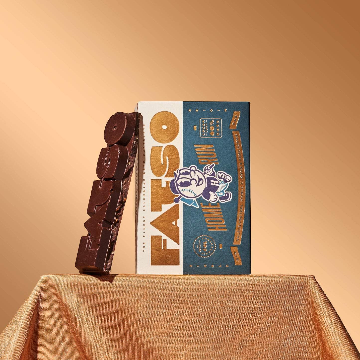 Fatso Home Run 60% dark chocolate slab with pretzel, honeycomb, and almond inclusions next to its branded packaging.