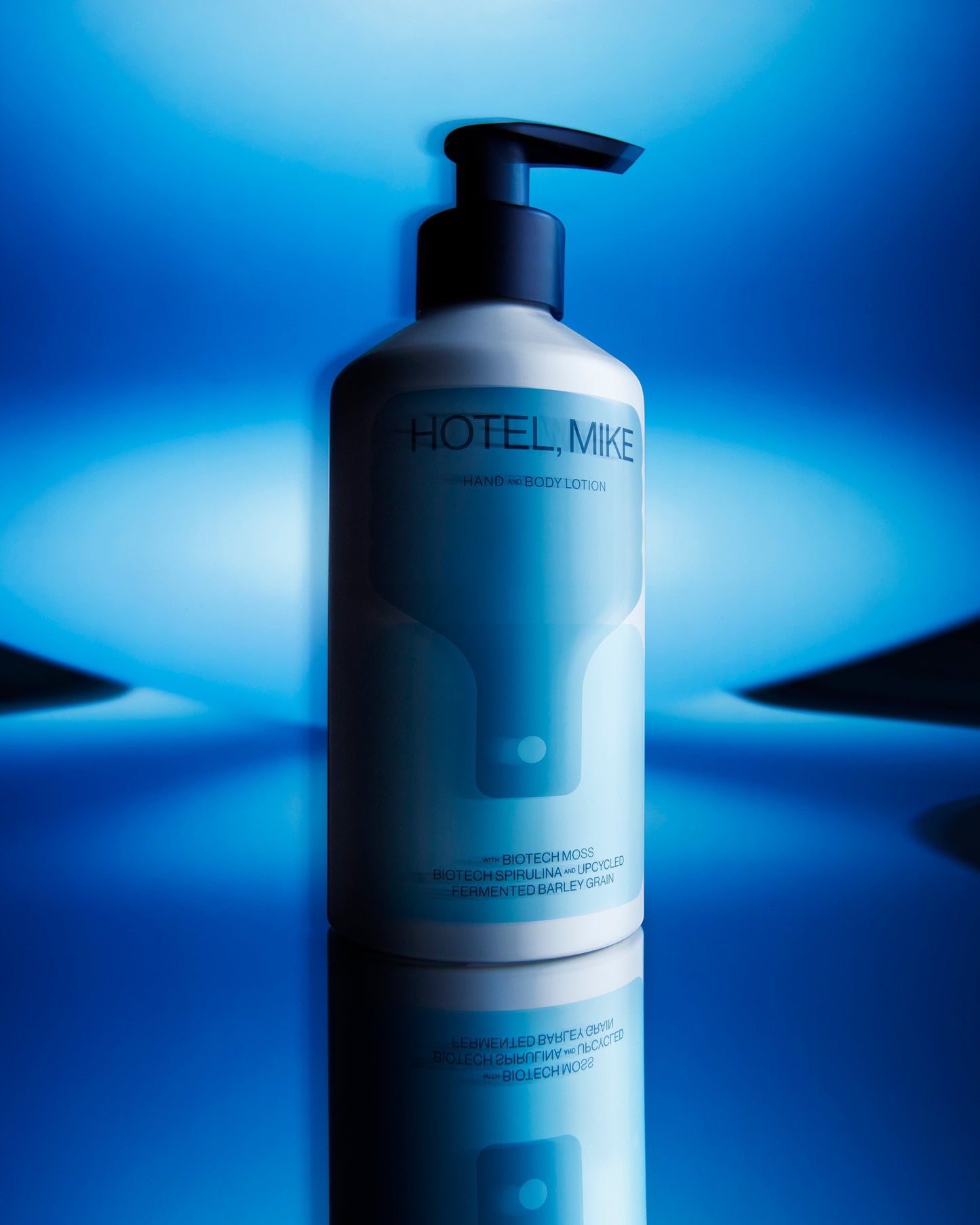 Hotel, Mike hand and body lotion in a sustainable aluminium bottle against a vibrant blue studio background.
