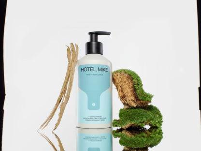 Hotel, Mike hand and body lotion in an aluminium bottle with moss and bark accents on a reflective surface.