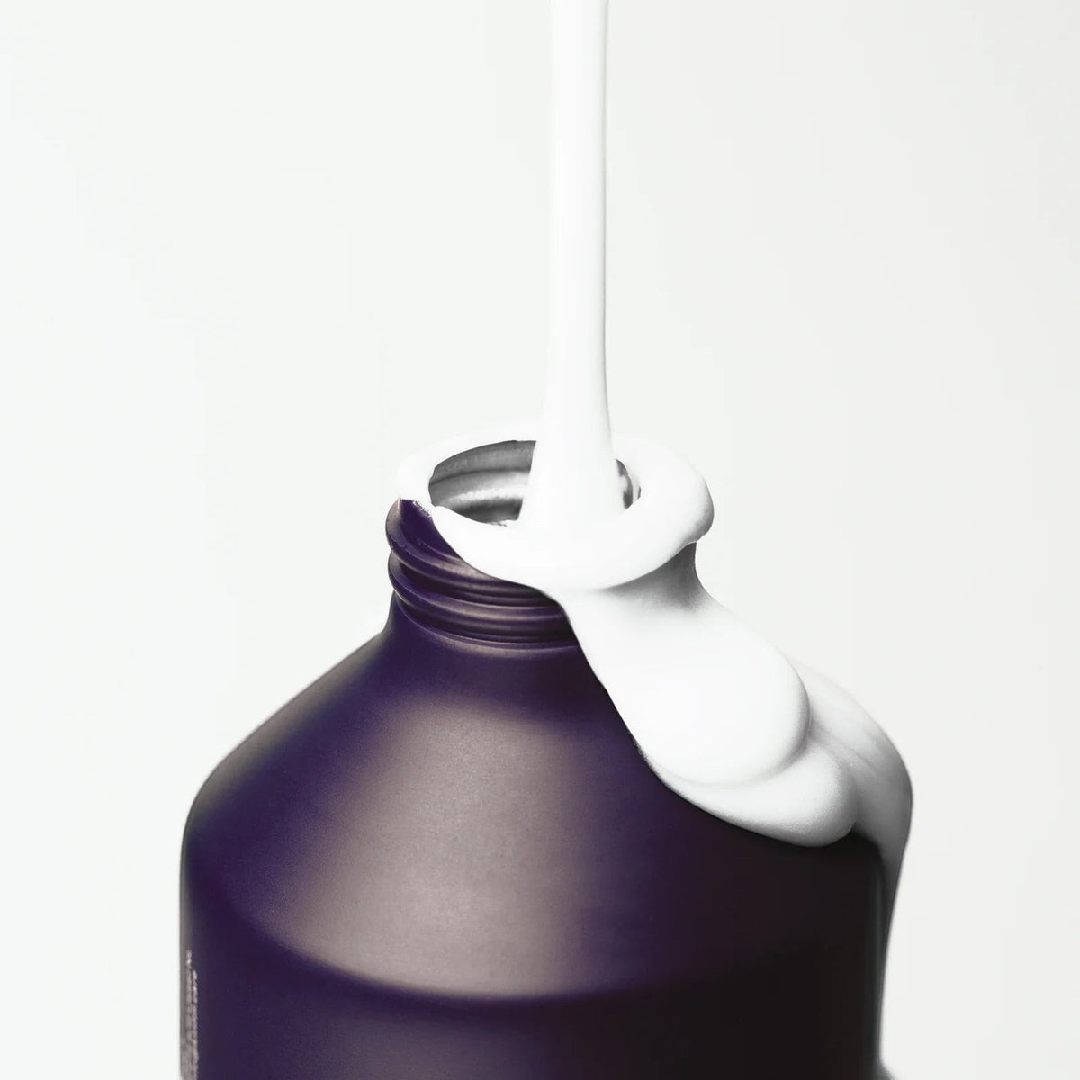 Kinfill body lotion pouring from a refillable dark purple bottle, showcasing a rich white cream texture.