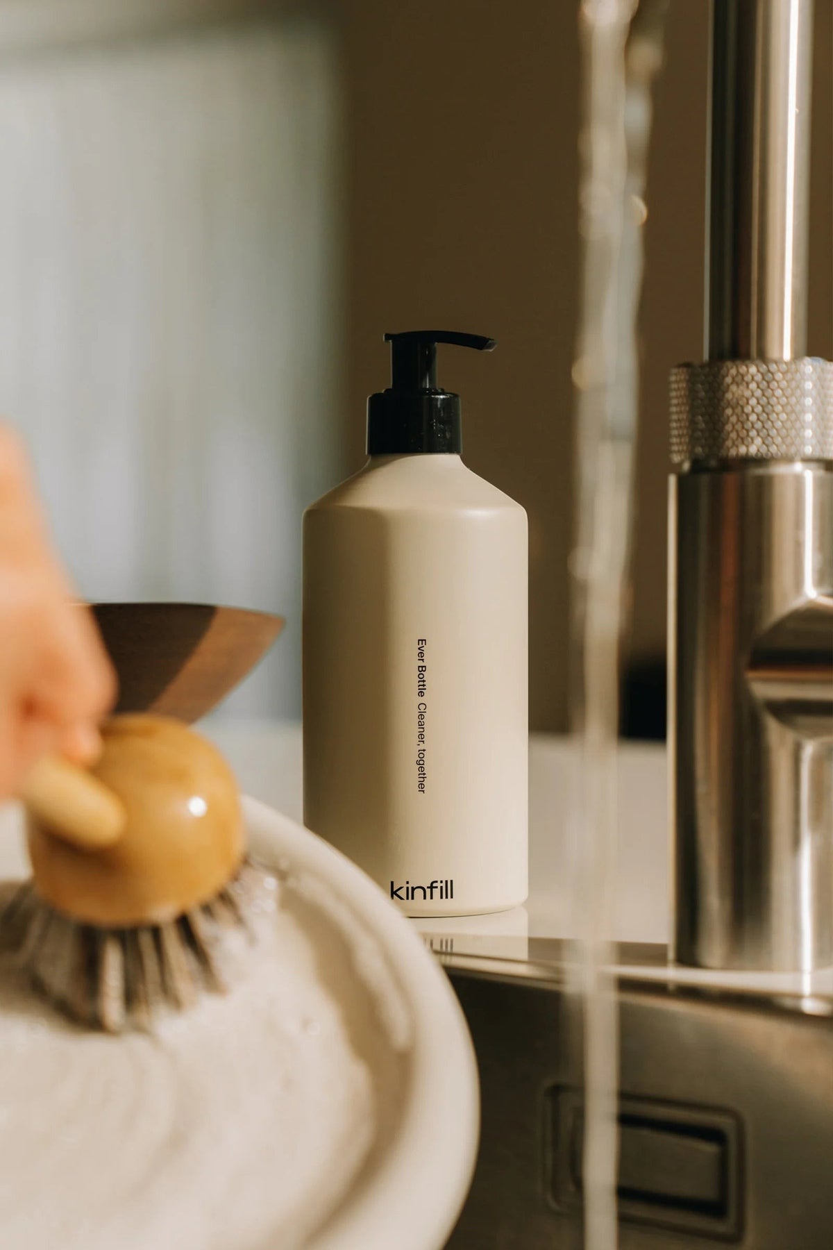 Kinfill dish soap refill bottle in a minimalist kitchen setting with a wooden dish brush and running water