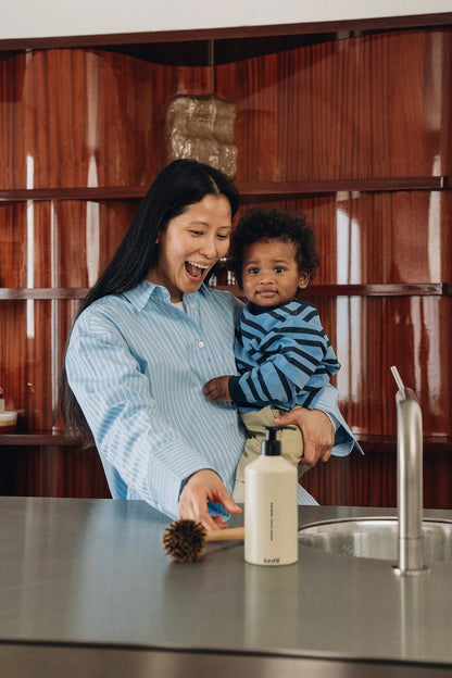Kinfill dish soap bottle on a kitchen counter with a woman holding a baby in a modern home setting