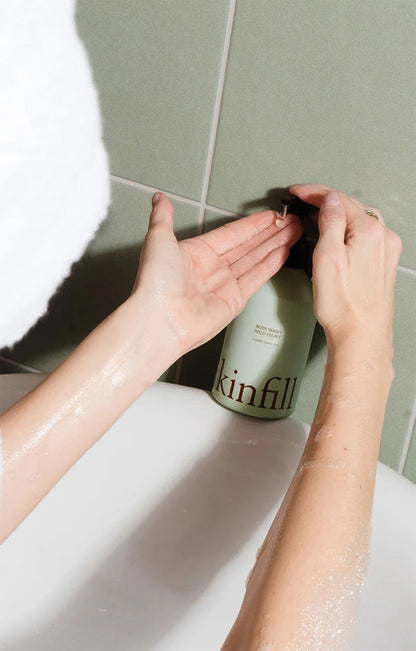 Kinfill Wild Peony body wash being dispensed from a refillable aluminium bottle into hands in a tiled bathroom
