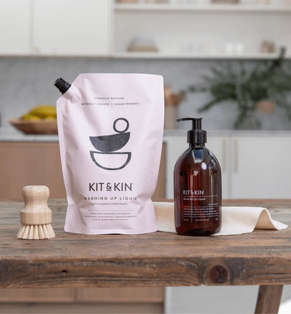 Kit & Kin eco-friendly washing-up liquid refill pouch and amber pump bottle with a wooden dish brush on a table.