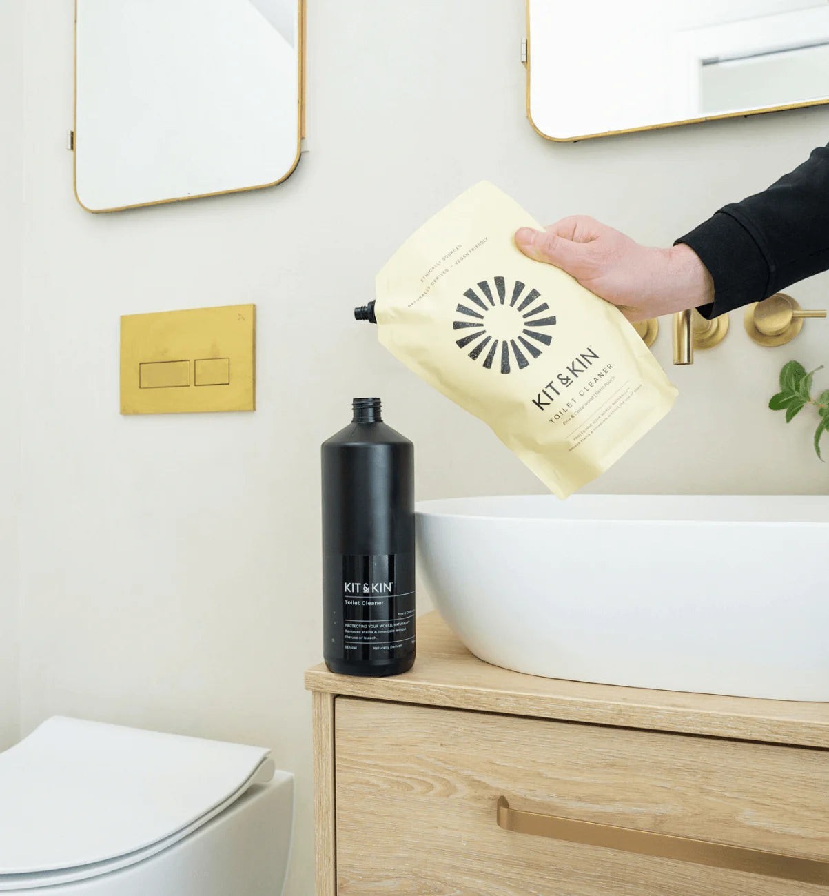 Kit & Kin plant-based toilet cleaner refill pouch being poured into a black bottle in a modern bathroom