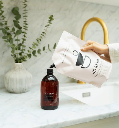 Kit & Kin eco-friendly washing-up liquid refill pouch being poured into a reusable amber glass bottle