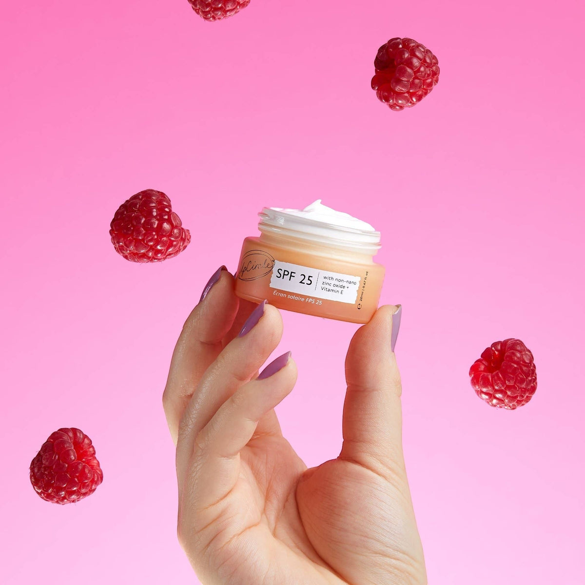 UpCircle SPF 25 mineral sunscreen jar held in hand against a pink background with floating raspberries