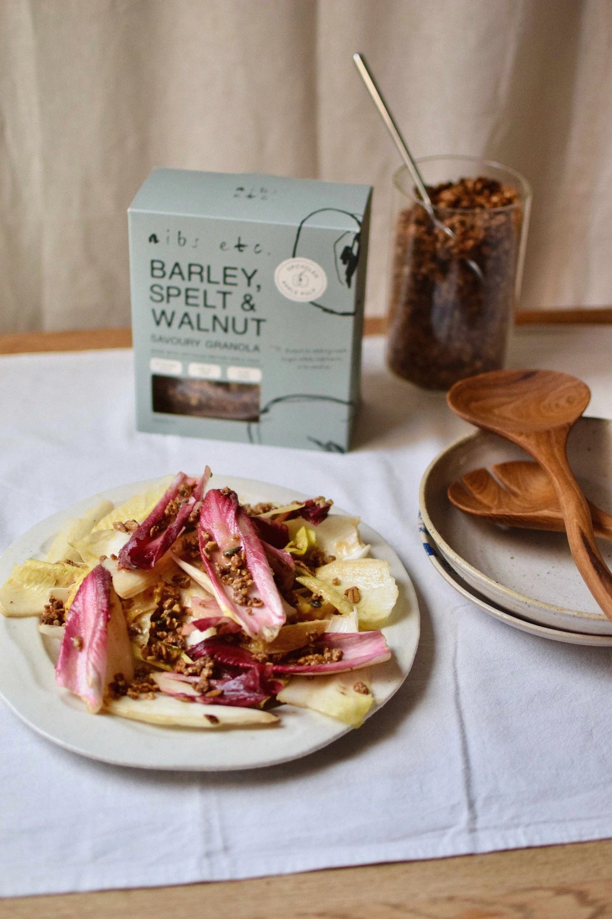 Nibs Etc. savoury granola with barley, spelt, and walnuts sprinkled over a fresh chicory salad on a plate.