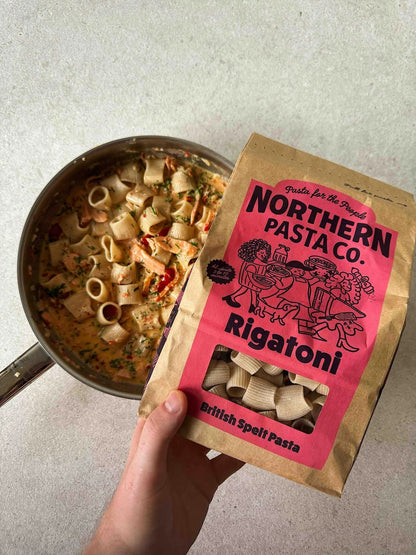 Northern Pasta Co. Rigatoni in a brown paper bag next to a pan of creamy pasta with vegetables