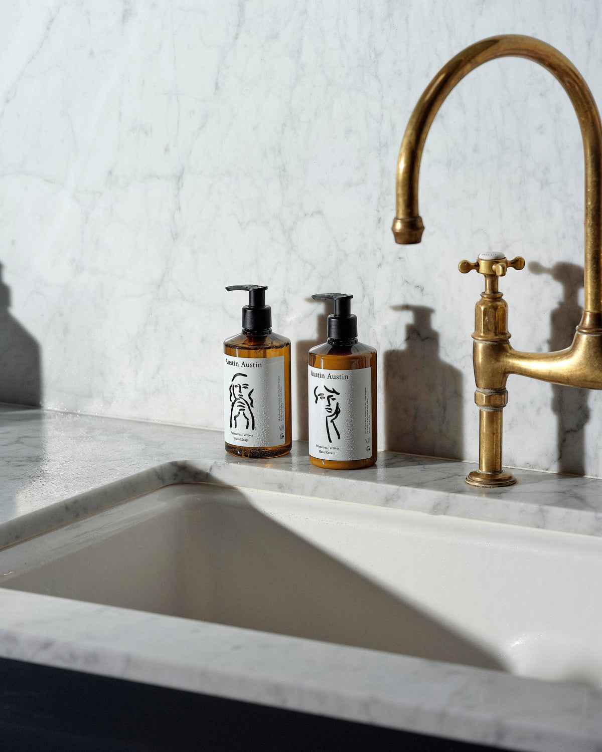 Austin Austin Palmarosa & Vetiver hand cream and soap bottles with Christian Newby ink art on a marble sink counter.