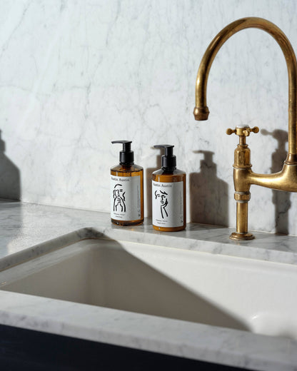Austin Austin Palmarosa & Vetiver hand cream and soap bottles with Christian Newby ink art on a marble sink counter.
