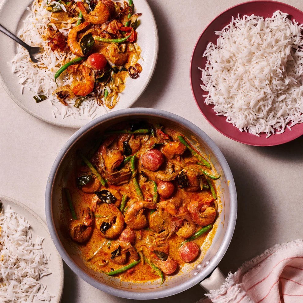 Nice Rice Pure Basmati Rice served with a fragrant prawn curry and vegetables in a top-down kitchen table setting.