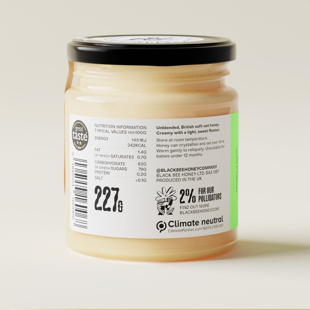 Black Bee Honey Raw British Spring Honey in a glass jar with a cream-coloured soft-set texture and detailed product label.
