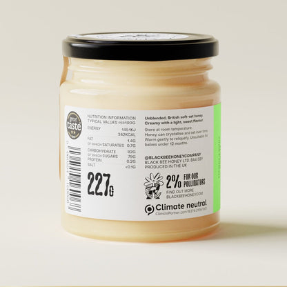 Black Bee Honey Raw British Spring Honey in a glass jar with a cream-coloured soft-set texture and detailed product label.